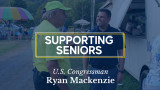 Congressman Mackenzie talks with a man at a fair. Caption: Supporting Seniors